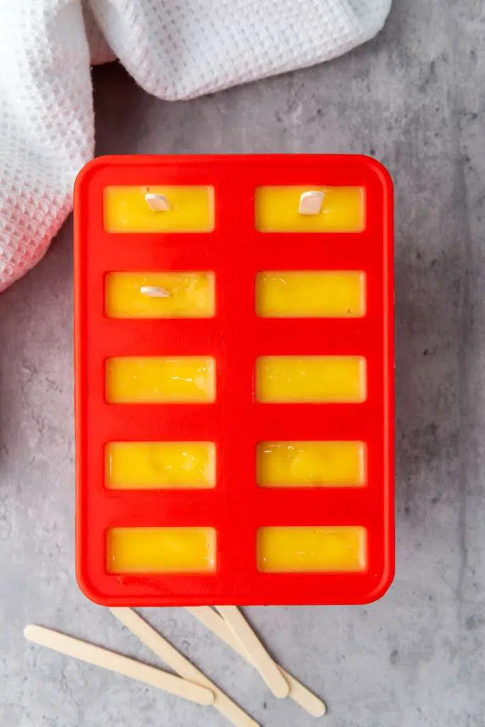 Delicious Tropical Mango Coconut Lime Popsicle Recipe Mango lime popsicles in a popsicle mold with a few stick inserted.