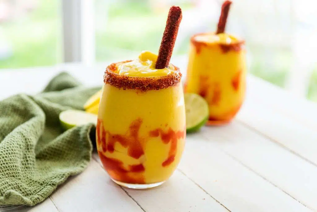 Two glasses of mangonada, a mexican mango drink, with tamarind candy straws as garnish.