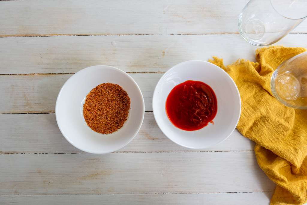 Ingredients to rim the mango chamoyada glasses - tajin seasoning and chamoy sauce in small white bowls.