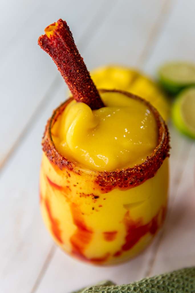 Mangonada with a tamarind candy stick in a tall rimmed glass.