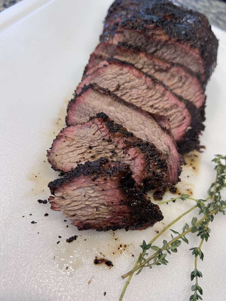 Sliced Coffee Rubbed Tri-Tip on a white cutting board with fresh thyme sprigs for garnish.