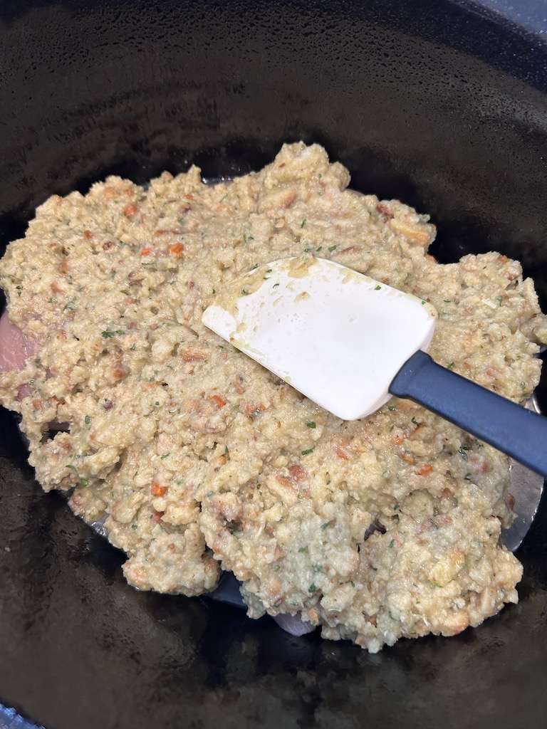 Spreading the stuffing mixture with a spatula over the chicken breasts in the slow cooker.