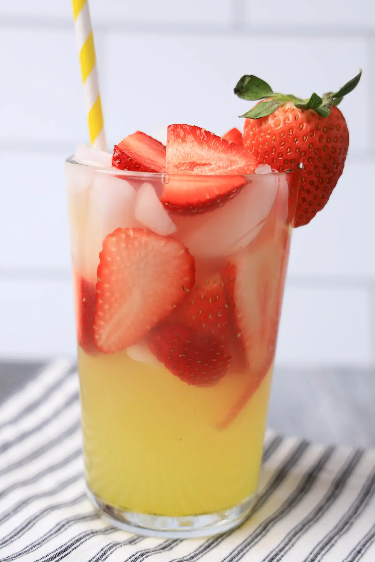 Iced strawberry lemonade in a glass with fresh slices and a yellow striped straw