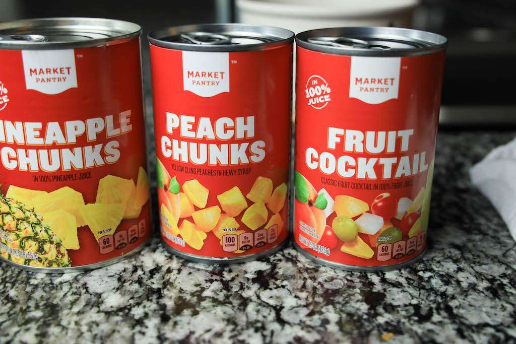 Three cans of fruit cocktail on the counter for ambrosia salad without coconut.