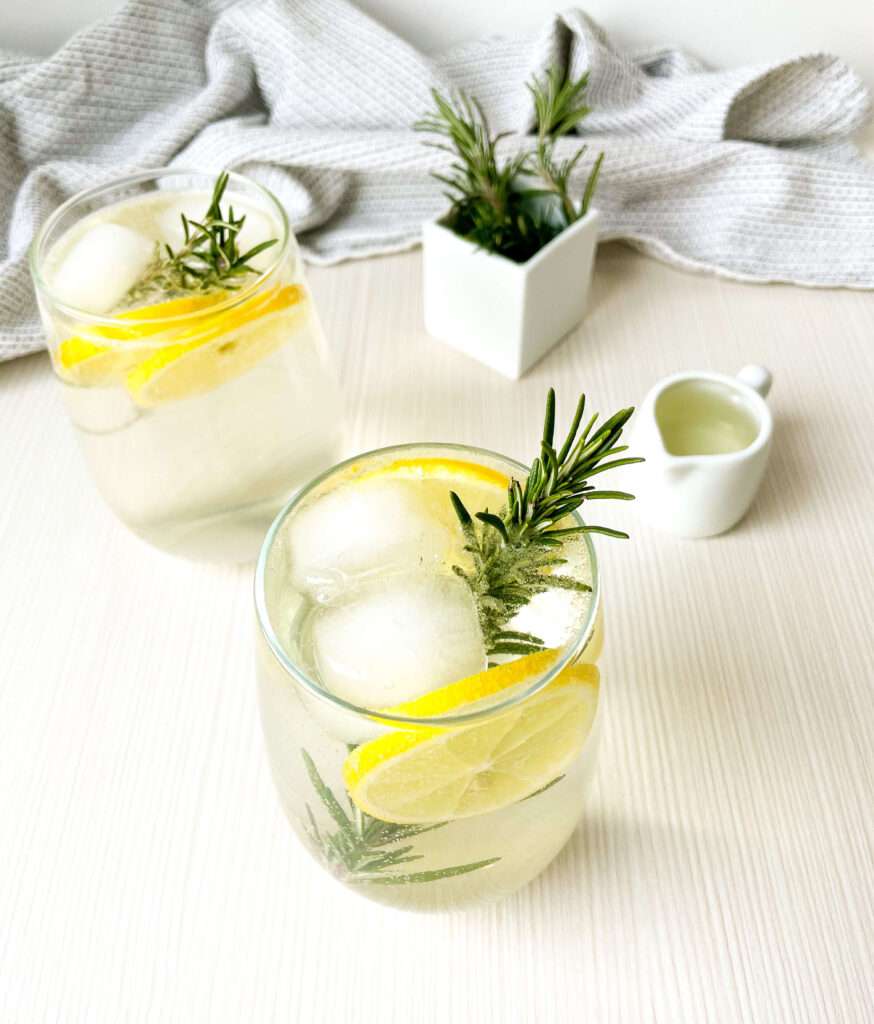 Two glasses of apple gin fizz garnished with fresh rosemary and lemon slices.