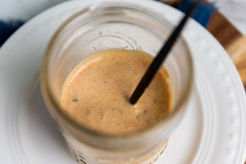 Looking into a glass mason jar half filled with homemade big mac sauce with a black spoon.
