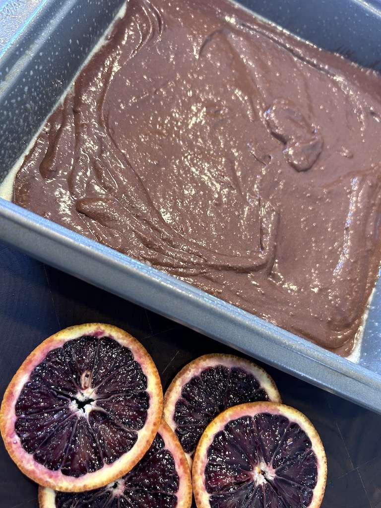 Blood orange brownie batter in a baking pan with sliced blood oranges