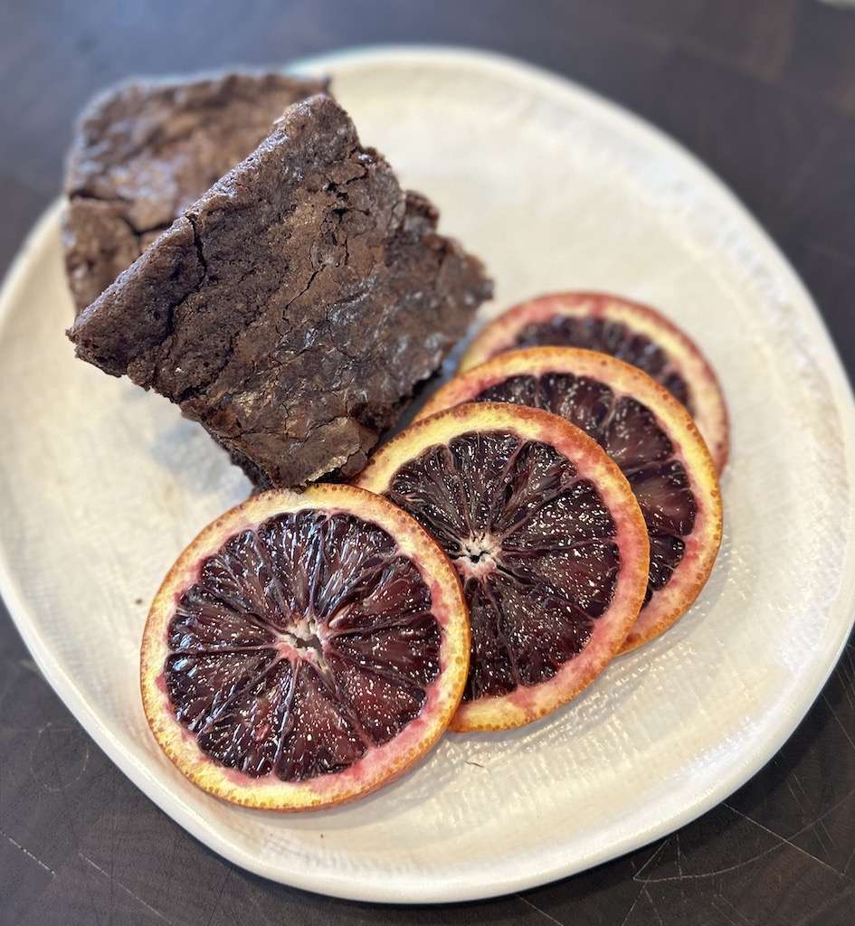 Two blood orange brownies on a white plate with four slices of blood orange.
