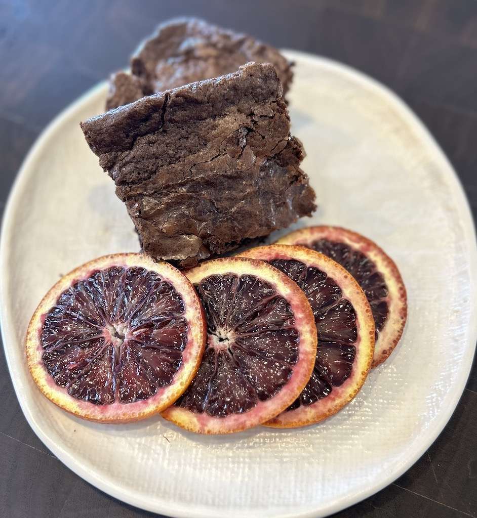 Two delicious blood orange brownies on a white plate with slices of fresh blood oranges.