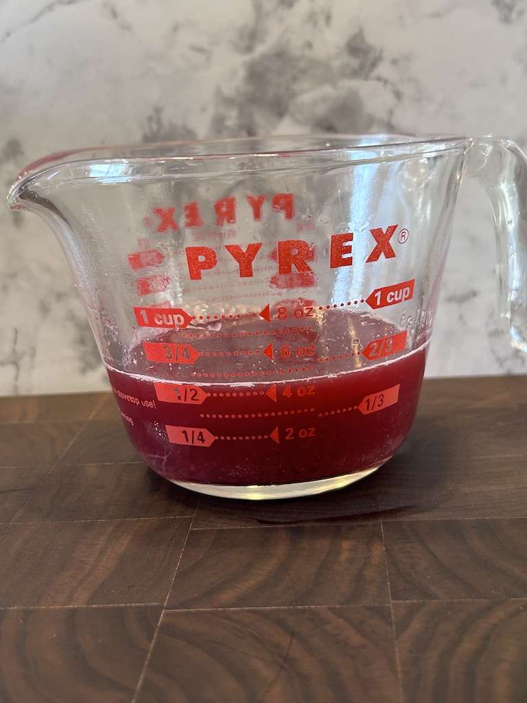 A glass measuring cup full of freshly squeezed blood orange juice to make blood orange simple syrup.