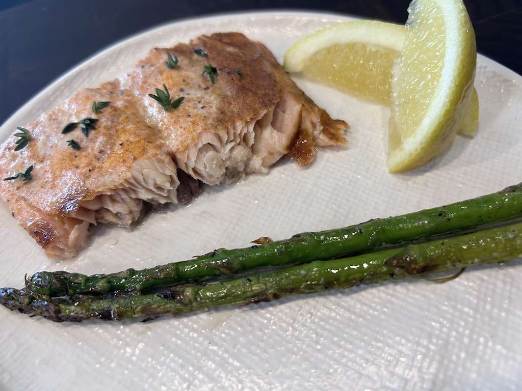 A serving of Kamado Joe cedar planked salmon on a plate with fresh lemon slices and grilled asparagus.