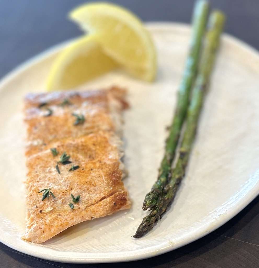 The perfect salmon side dish of grilled asparagus on a white plate with salmon and lemon wedges.