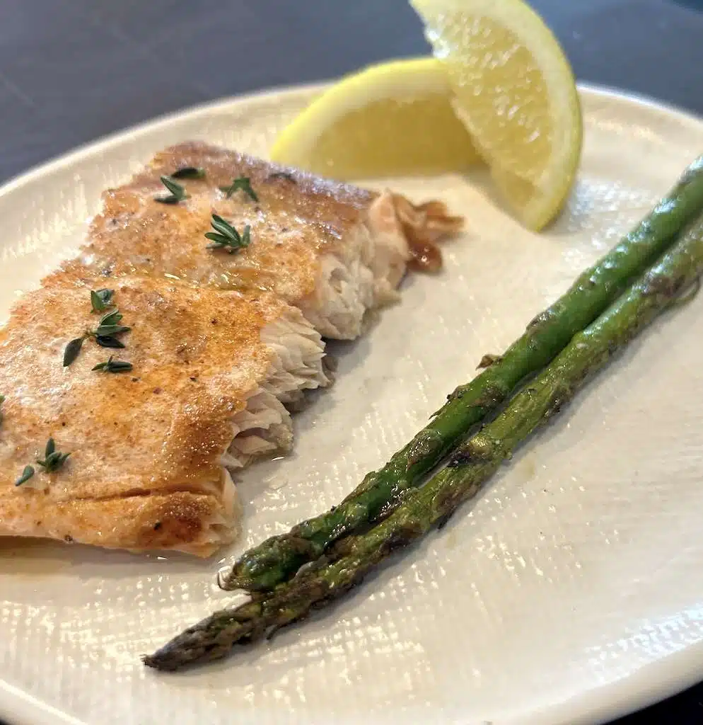 A serving of cedar planked salmon with fresh lemon wedges and grilled asparagus on a white plate.