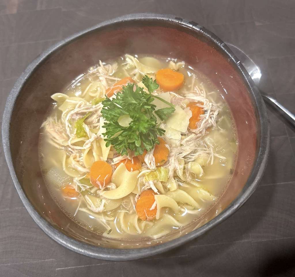 A bowl of chicken noodle soup garnished with fresh parsley.