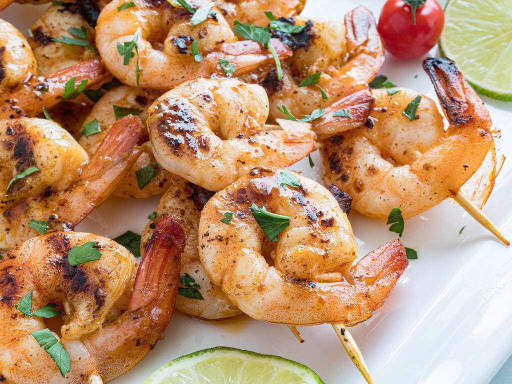 Chipotle Lime Shrimp Kabobs on a white plate with fresh lime slices and parsley as a garrnish.