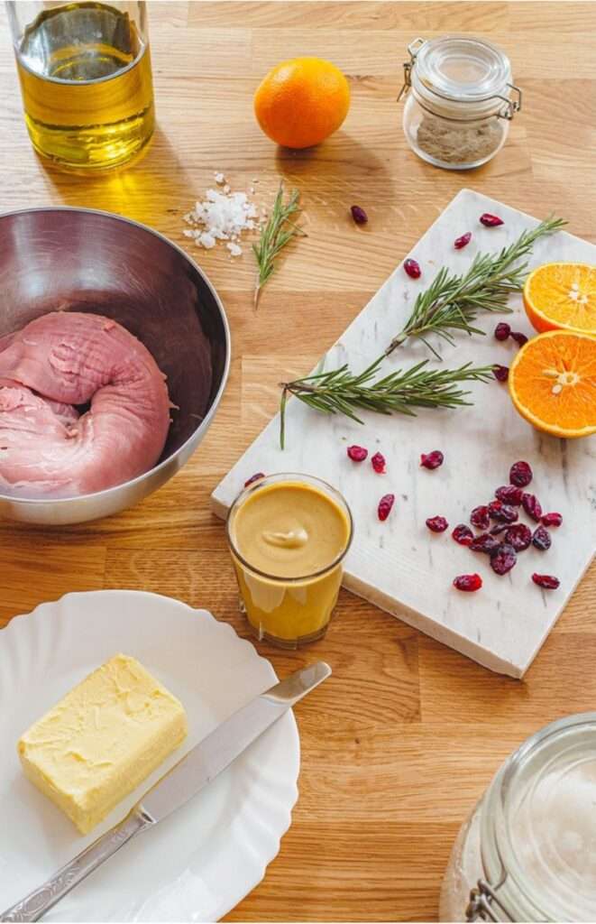 The ingredients for orange cranberry pork tenderloin including dried cranberries, oranges, a pork tenderloin, butter and fresh rosemary.
