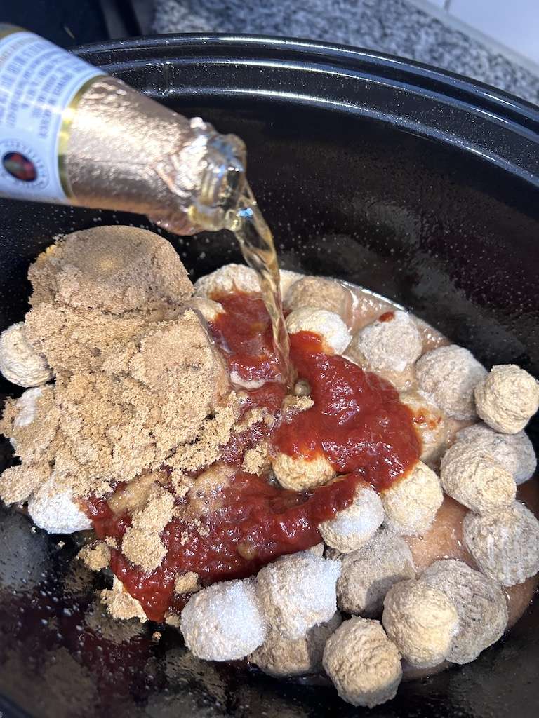 Adding the beer to the crockpot for drunken chili meatballs.