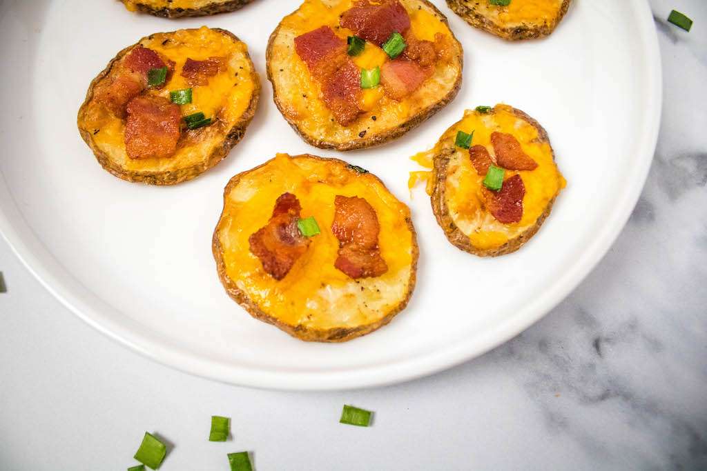 Air fryer loaded potato slices on a white plate garnished with fresh chopped chives ready for serving.