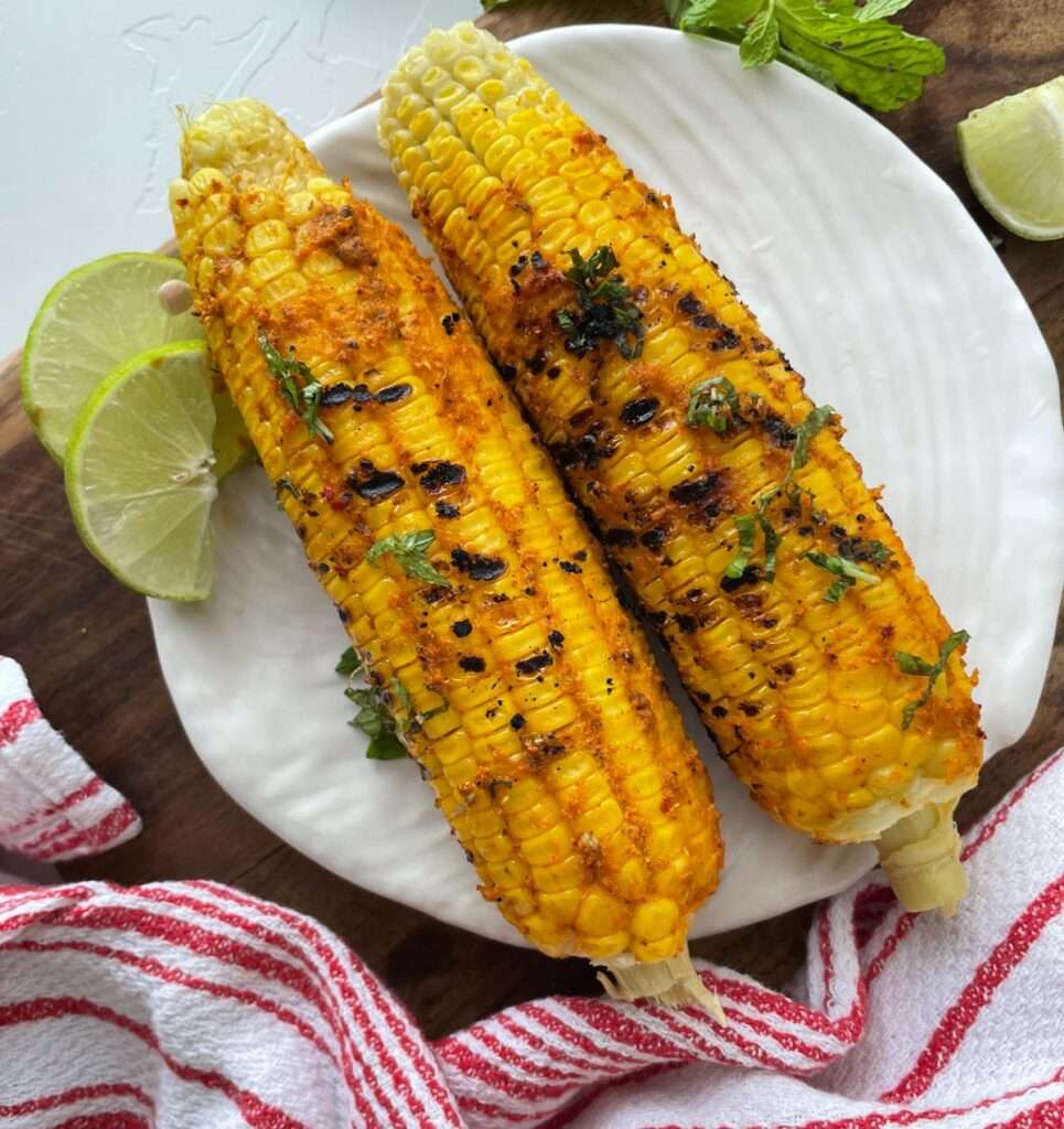 Spiced grilled corn on the cob with cilantro and lime wedges
