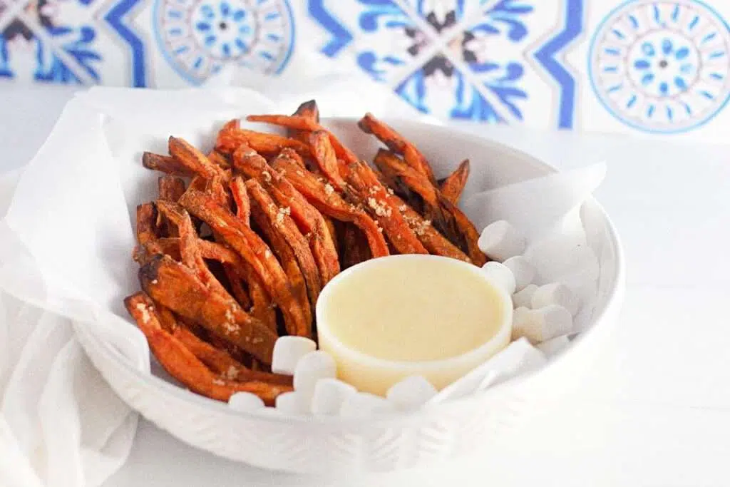 Crispy sweet potato fries with aioli dip in a white bowl