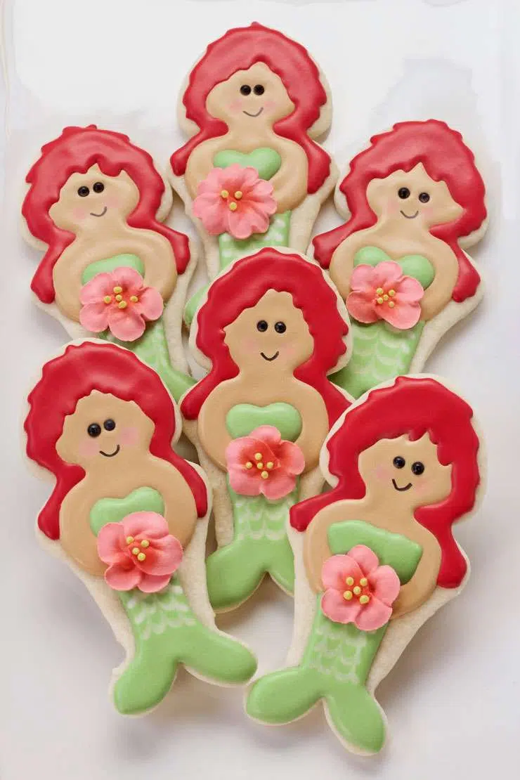 Mermaid sugar cookies with red hair, green tails, and pink royal icing flowers