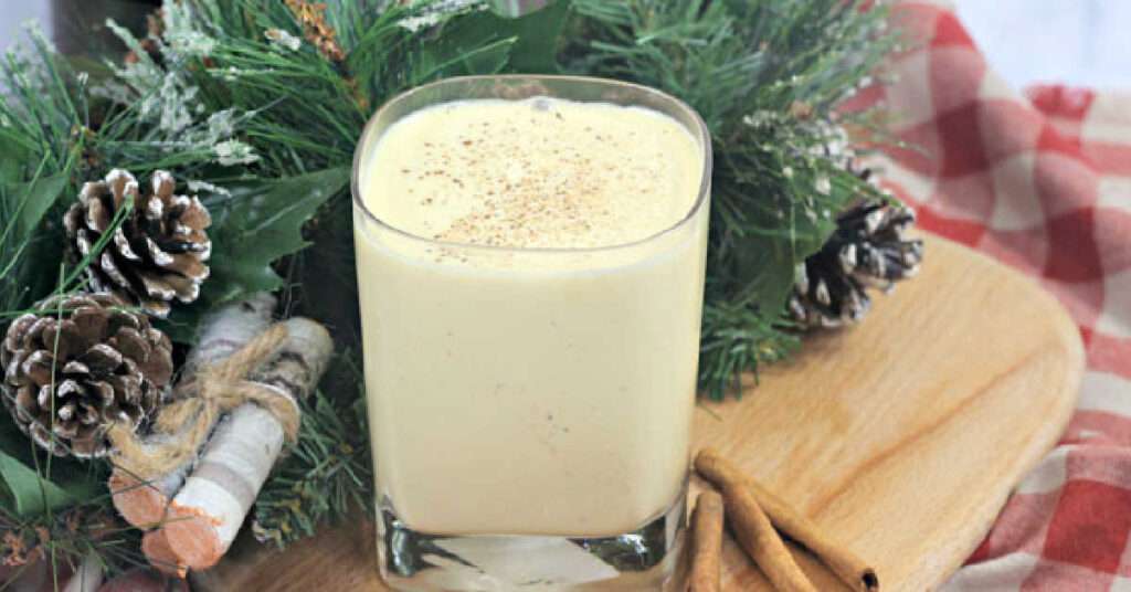 Glass of eggnog with nutmeg and cinnamon, holiday drink by pine decor.