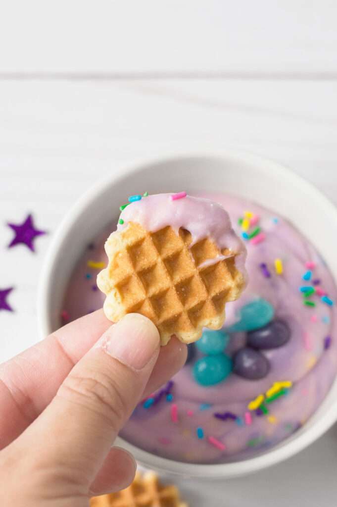 10 of the Cutest Mermaid Cookie Recipes Hand holding mini waffle cookie dipped in purple frosting with sprinkles