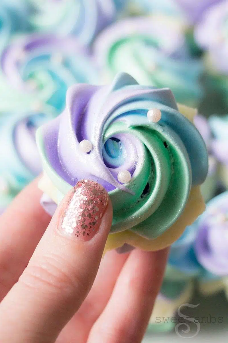 Close-up of hand holding pastel swirl meringue cookie with pearl sprinkles