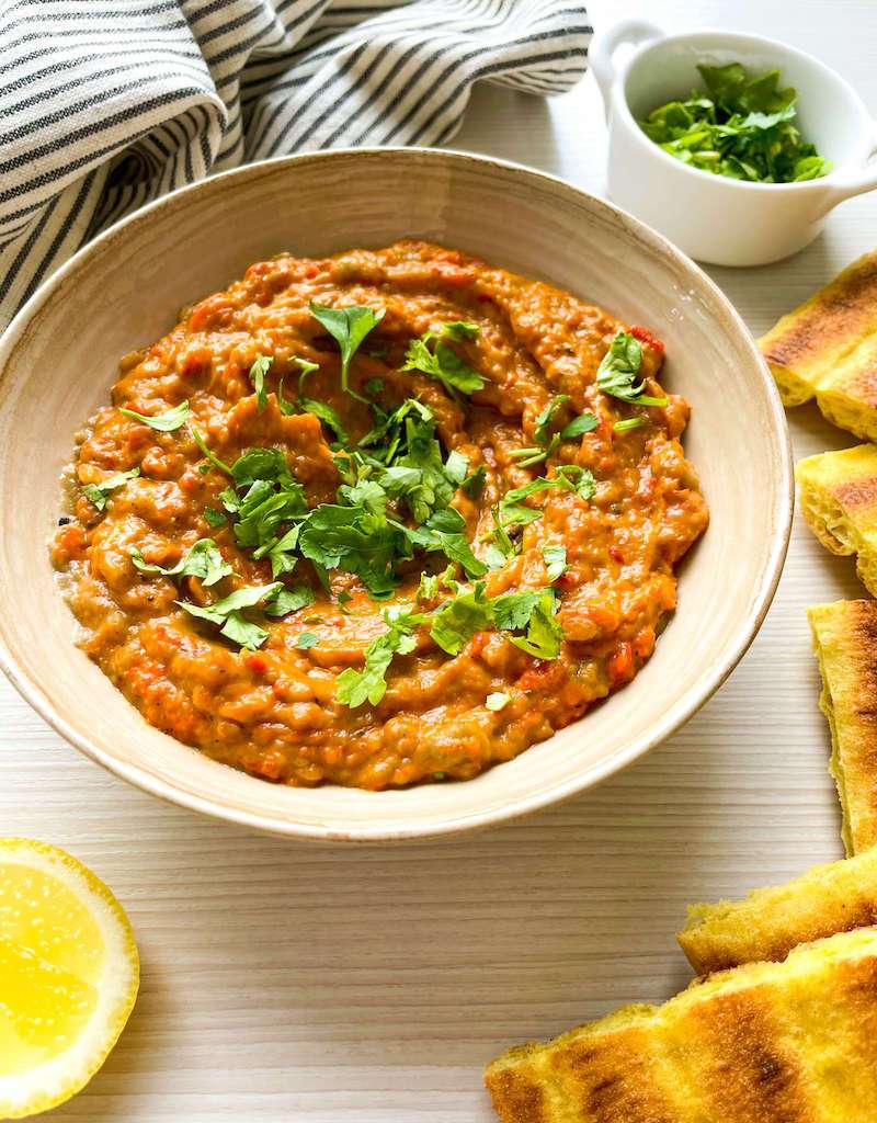 A bowl of moroccan eggplant dip surrounded by toasted bread for dipping and a fresh lemon half.
