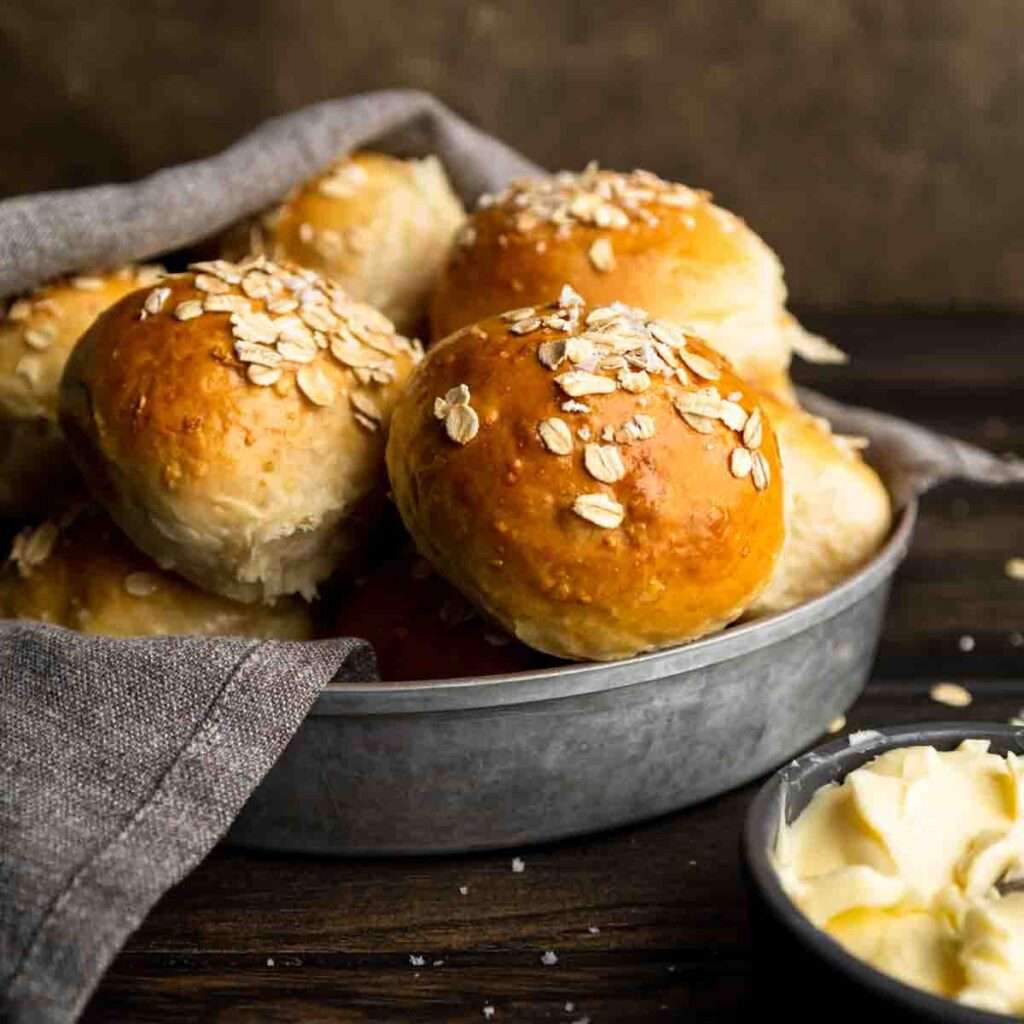 Homemade golden oat-topped dinner rolls in a pan with butter