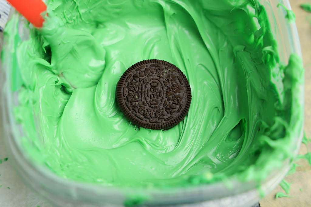 Dipping an Oreo cookie into the melted green candies to make the body of the cute frog cookies.