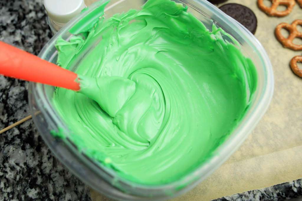 Melted green candies in a Tupperware container with a plastic spatula to make frog cookies.