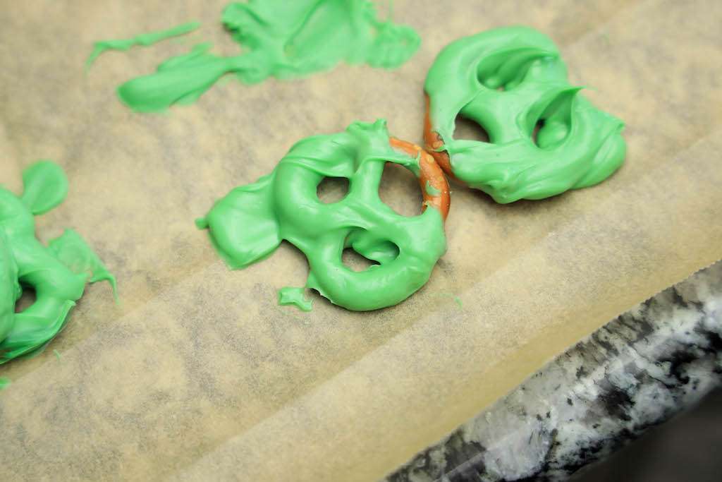 Pretzels dipped in melted green candies to make Oreo frog cookies on parchment paper.