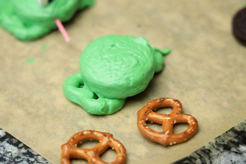 Assembling the Oreo Frog cookies by placing the green candy dipped Oreo on top of the frog pretzel cookie legs.