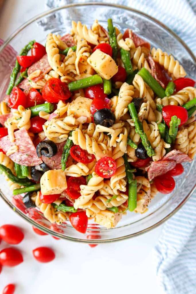 Italian rotini pasta salad with tomatoes, olives, asparagus, salami and cheese cubes
