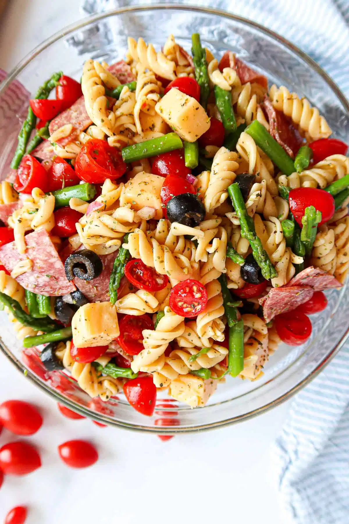 Italian rotini pasta salad with tomatoes, olives, asparagus, salami and cheese cubes