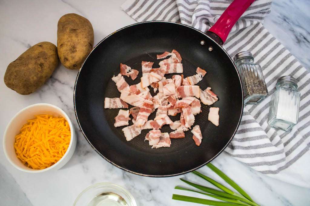 Frying the bacon in a skillet to add to the air fryer potato slices.