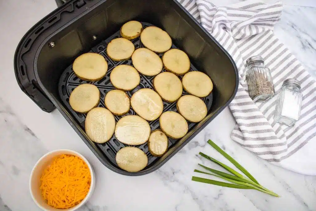 The olive oil brushed potato slices layered in the air fryer with the topping ingredients near by.