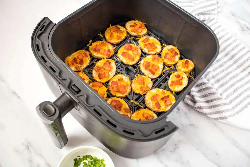 The air fryer potato slices with melted cheddar and crispy bacon in the air fryer.