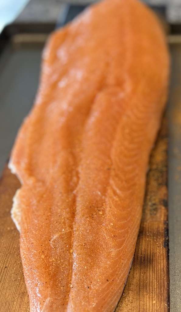 A seasoned salmon fillet on a cedar plank ready to go on the Kamado Joe.