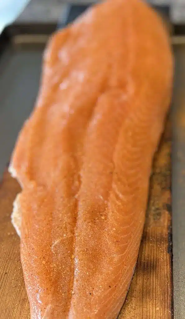 A seasoned salmon fillet on a cedar plank ready to go on the Kamado Joe.