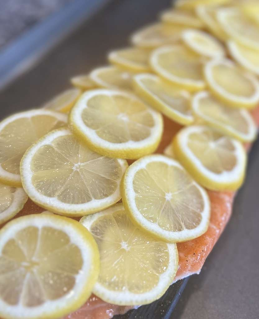 Lemon slices on top of a salmon fillet on a cedar plank.