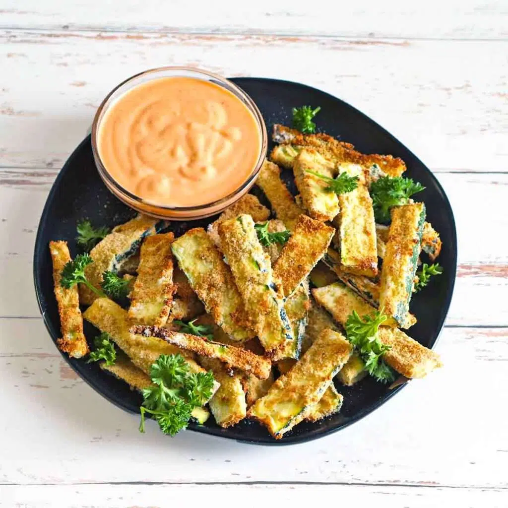 Crispy baked zucchini fries with creamy dipping sauce on plate