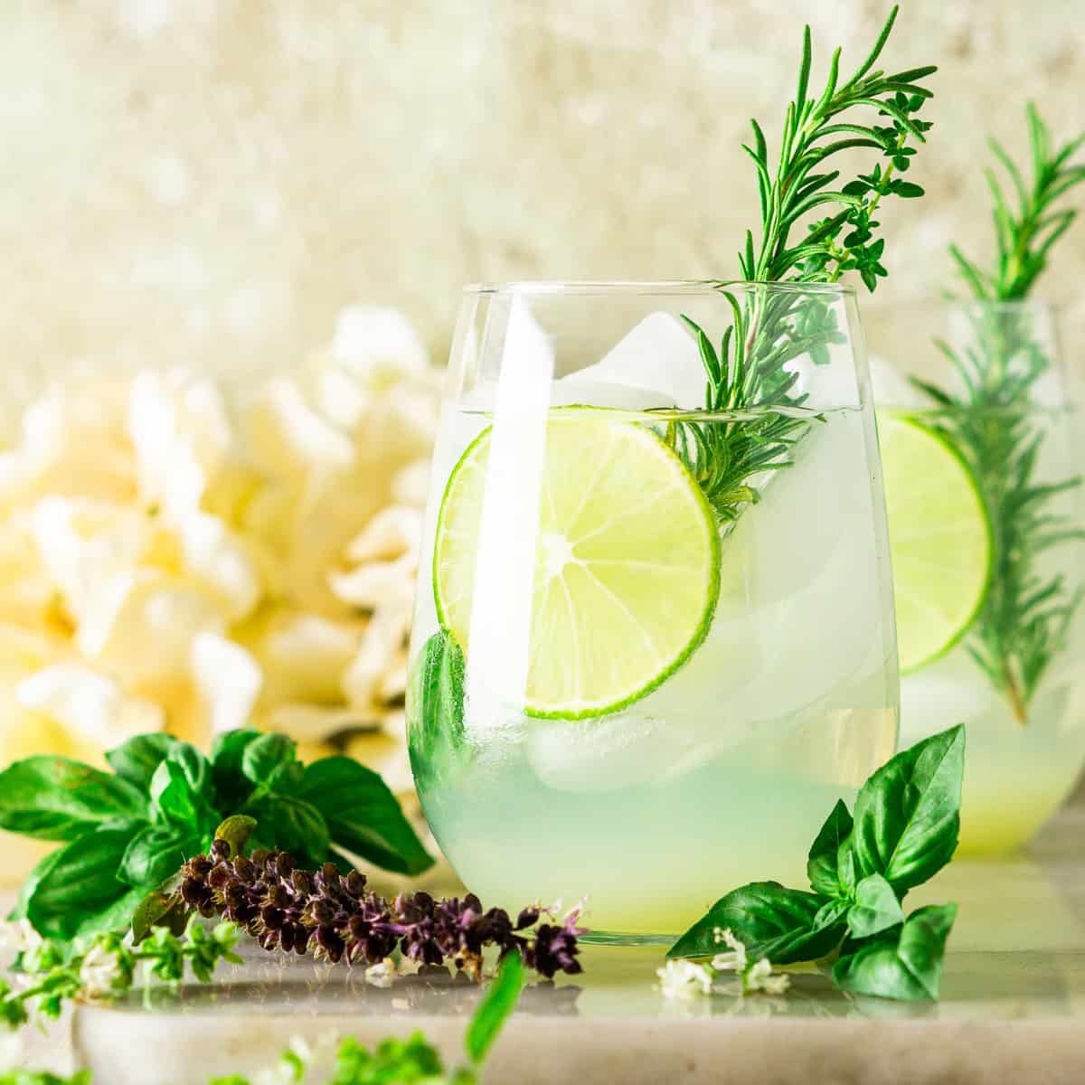 Garden gin and tonic in a glass with fresh lime slices and rosemary leaves.