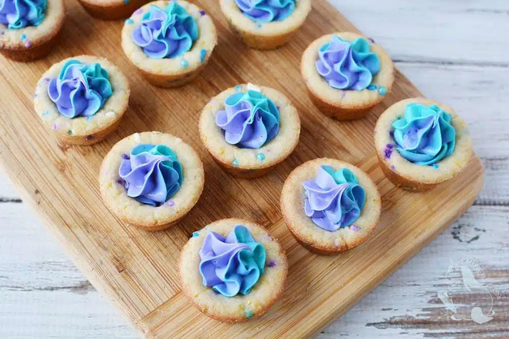 Sugar cookie cups with purple and teal buttercream rosettes on board