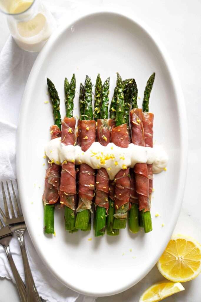 Prosciutto-wrapped asparagus with creamy sauce and lemon zest on platter