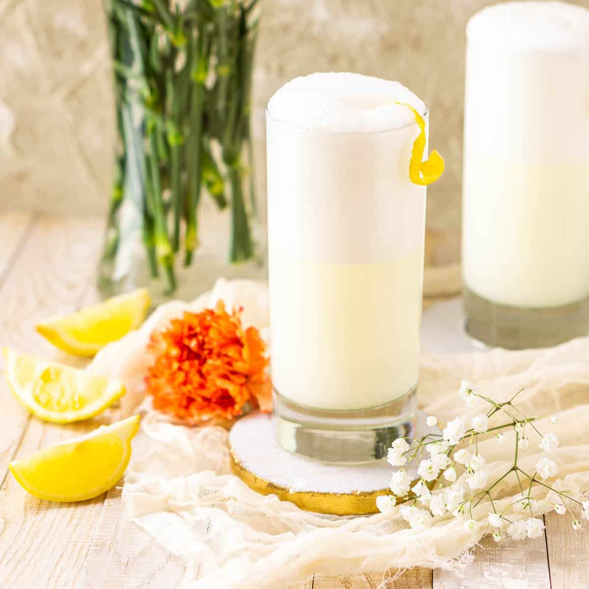 A ramos gin fizz in a tall glass with a fresh lemon peel curl for garnish.