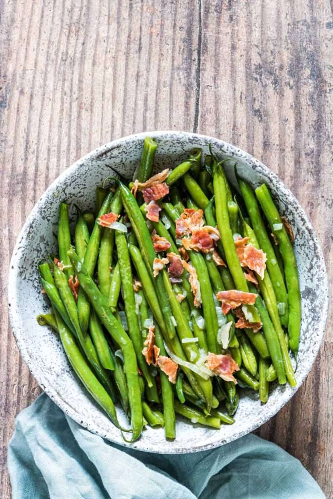 Sauteed green beans with bacon and onions in a rustic bowl
