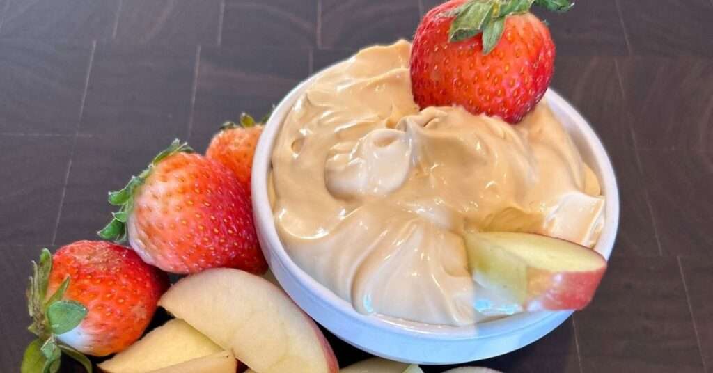 2 ingredient fruit dip with strawberries and apple slices in a white bowl on a wooden cutting board.