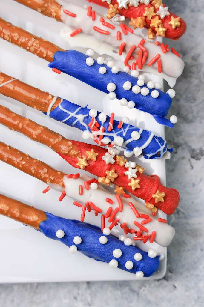 Patriotic pretzel rods including red, white and blue with sprinkles on a white plate.